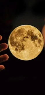 Hands holding an illuminated moon against a dark background.