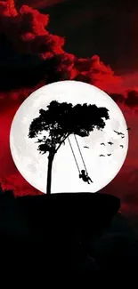 Silhouette of a swing on a tree with a red moonlit background.