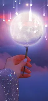 Hand holding glowing moon against purple night sky with clouds.