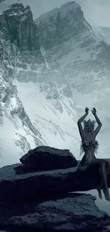 Mystical figure sits on rocks with snowy mountains in the background.