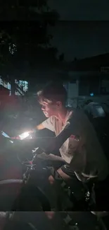 Cyclist illuminated by phone light during nighttime ride.