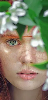 Red-haired woman with green eyes amidst white flowers and green leaves.