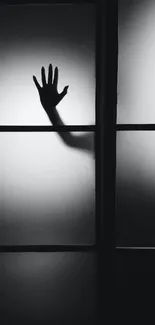 Mysterious silhouette of a hand behind a paneled glass in grayscale.