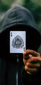 A hooded figure holding an ace of spades card against a dark green background.