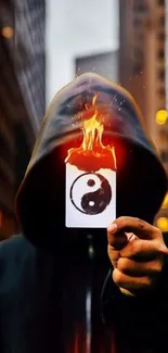 A hooded figure holds a flaming Yin Yang card in a cityscape at night.