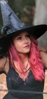 A witch with a black hat and pink hair against an autumn backdrop.