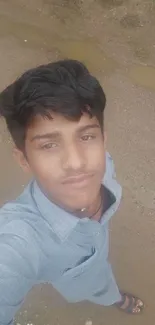 Boy takes a selfie outdoors on a dirt path, wearing a blue shirt.