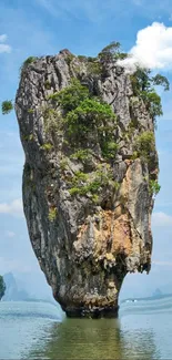 Towering rock formation against blue sky and sea in tropical landscape.