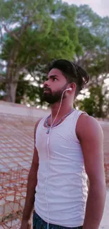 Man standing peacefully in nature, wearing white tank top and earphones.