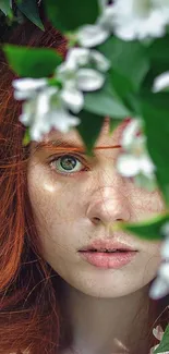 Serene face framed by green leaves and white flowers on a mobile wallpaper.