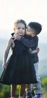 Children embracing on a hilltop with green hills in the background.