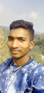 Man in blue shirt outdoors with nature background.