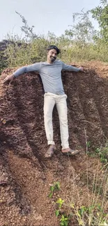 Man posing on a brown cliff with greenery in the background under a clear sky.