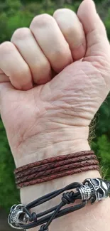 Fist with bracelets, greenery in background.