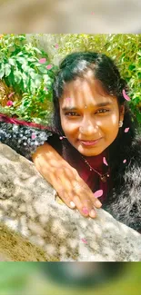 Smiling person outdoors with green foliage and sunlight.