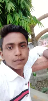 Young man in white shirt amidst lush greenery and wooden structures.