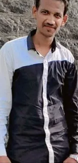 Man standing near a cascading waterfall on rocky landscape.