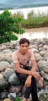 Person sitting on rocks by a serene river landscape.