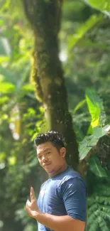 Man in blue shirt standing in lush green forest background.