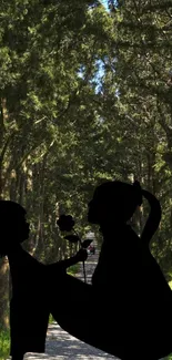 Silhouette of two figures on a forest path, surrounded by tall green trees.