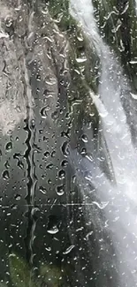 Raindrops on glass with waterfall view, creating a serene and natural mobile wallpaper.