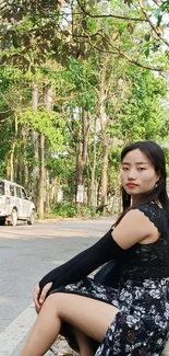 Woman sitting by forest roadside, scenic nature view.