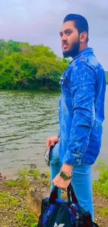 Man in blue denim beside tranquil lake with lush greenery.