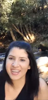 Woman smiling by a forest stream in nature scene.