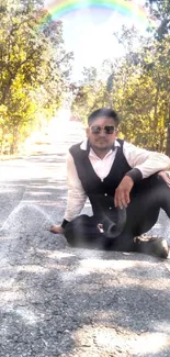 Man sitting on a nature-filled road under a rainbow.