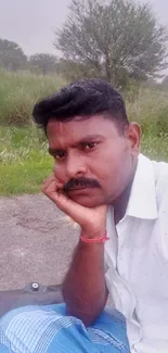 Man sitting outdoors in a green field, looking thoughtful.