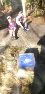 Children sitting on a rock in sunlit forest.