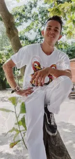 Person in white outfit posing outdoors under a tree.