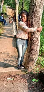 Person hugging a tree on a sunlit forest trail.