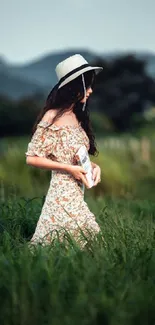 Woman in floral dress and hat walking through green fields.