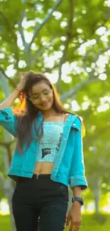 Woman in denim jacket walking among trees in sunlight.