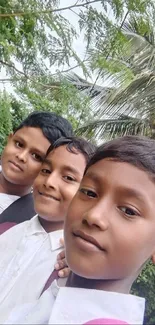 Three friends smiling under green trees.