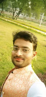 Man smiling in a lush green park with trees and grass around.