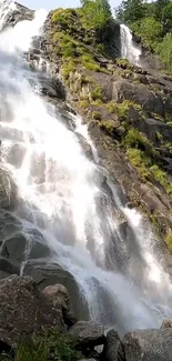 Cascading waterfall with rocks and greenery, perfect for mobile wallpaper.