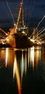 Navy ship docked at a night harbor with vibrant reflections on water.