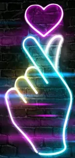 Vibrant neon hand forming a heart on brick wall.