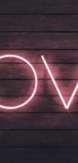 Neon love sign on dark wooden background with pink glow.