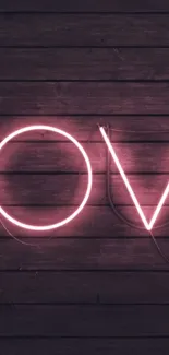 Neon love sign glowing against dark wooden background.