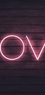 Neon love sign on dark wood wallpaper with pink glow.