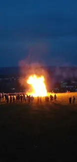 A bright bonfire in the night with people gathered around in a blue lit field.