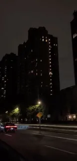 Dark city road with buildings illuminated by streetlights at night.