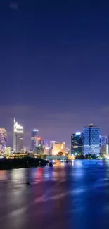 City skyline at night with reflections on the river and vibrant lights.