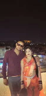 Couple on a rooftop with night city view.