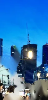 Night cityscape with skyscrapers illuminated against a blue sky.