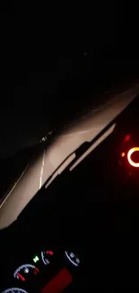 Nighttime view from a car dashboard on a dimly lit highway road.