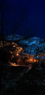 Night view of a mountain village with warm glowing lights and a dark blue sky.